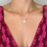 Collier en acier inoxydable doré maille perlée avec pendentif fleur en nacre, porté sur le décolleté d'une personne en haut