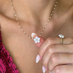Collier maille perlée en acier inoxydable doré, pendentif fleur en nacre tenu par un doigt. Une bague fleur assortie est au