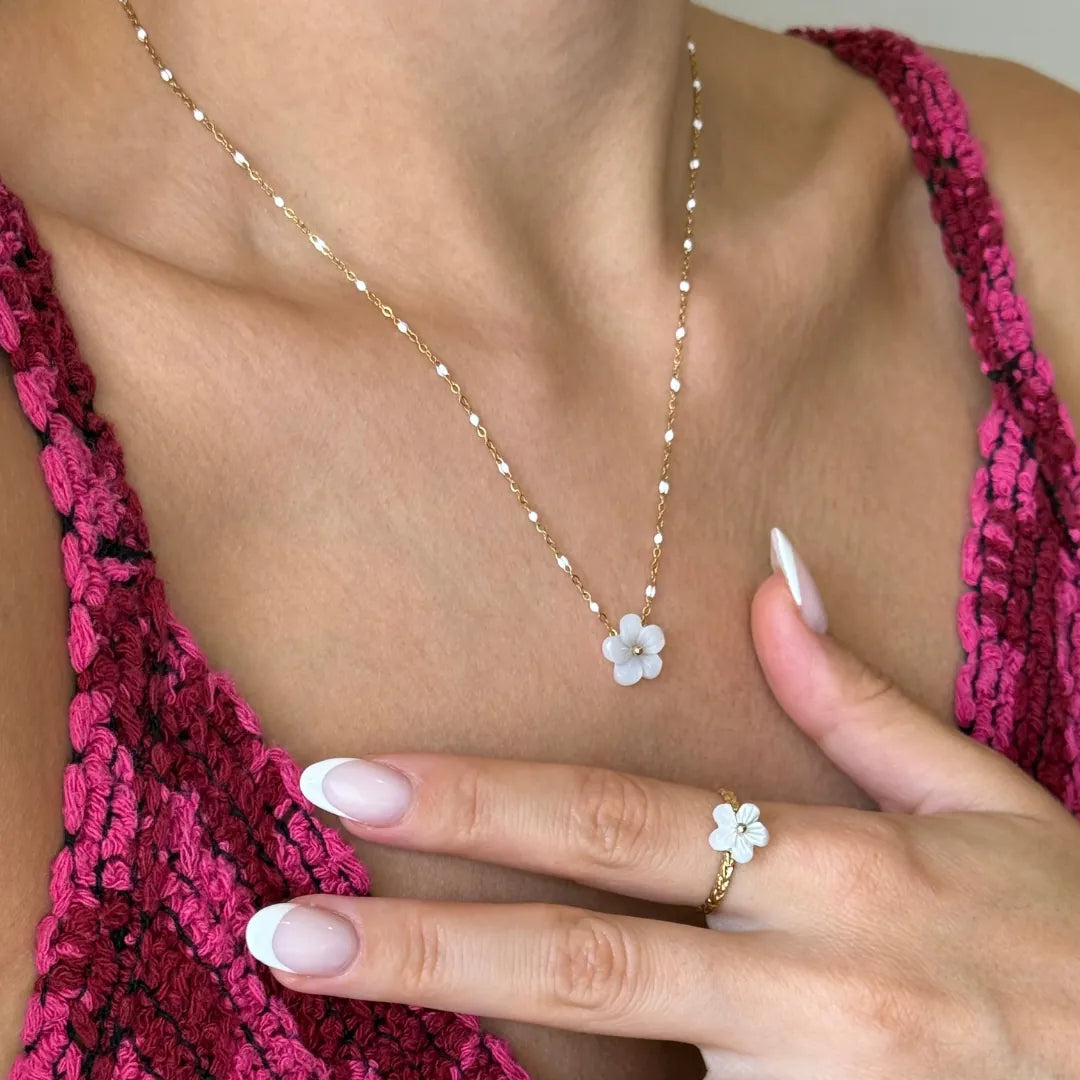 Collier et bague assortie en acier inoxydable doré à perles blanches et fleur en nacre, portés par une femme.