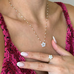 Collier et bague assortie en acier inoxydable doré à perles blanches et fleur en nacre, portés par une femme.