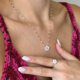 Collier et bague assortie en acier inoxydable doré à perles blanches et fleur en nacre, portés par une femme.