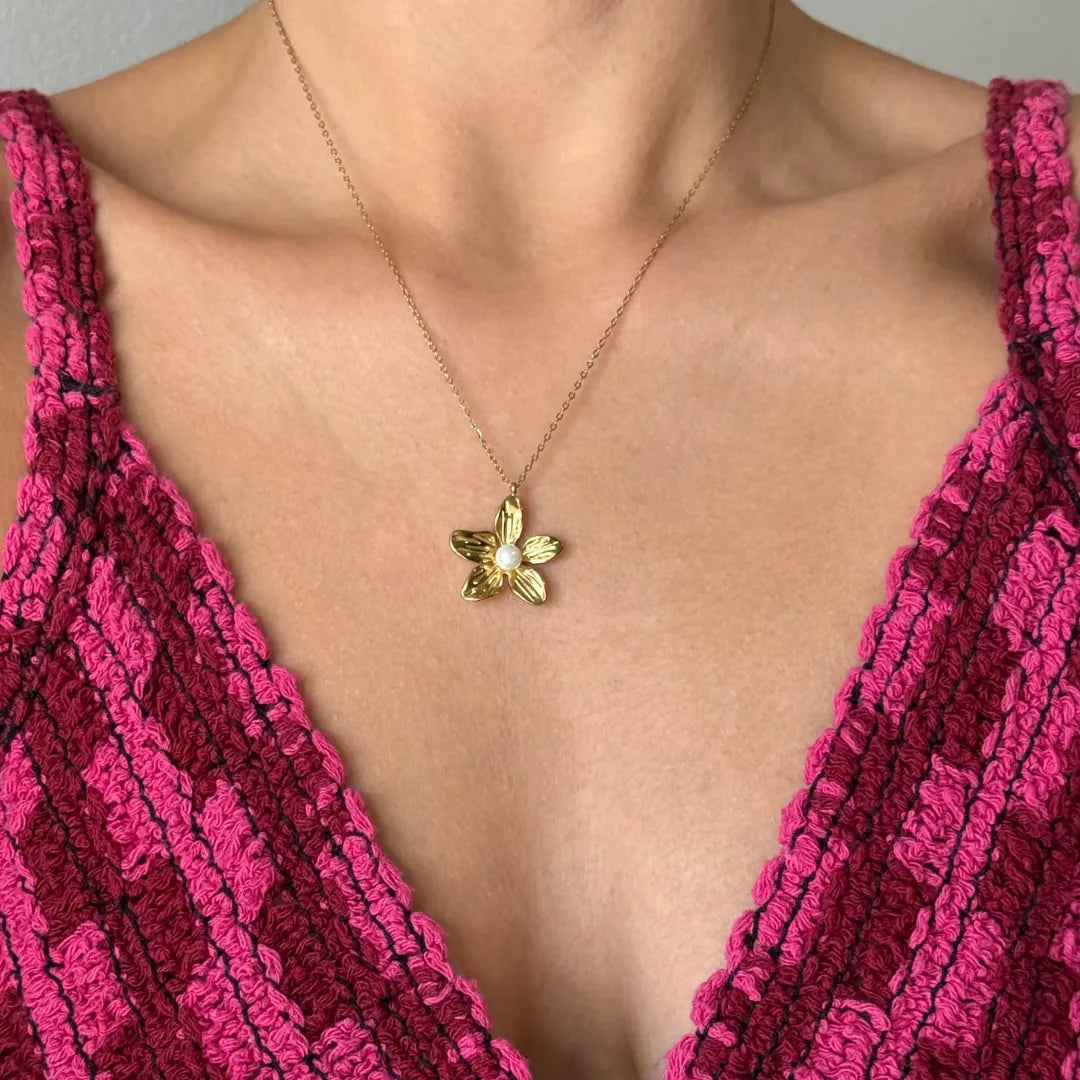 Collier acier inoxydable doré avec pendentif fleur et perle centrale sur le décolleté d'une femme.