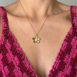 Collier acier inoxydable doré avec pendentif fleur et perle centrale sur le décolleté d'une femme.