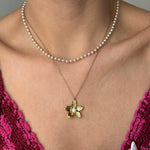 Collier acier inoxydable doré pendentif fleur avec perle, porté avec un collier ras-de-cou de perles blanches.