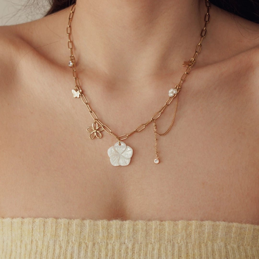 Collier en acier inoxydable doré, maillons, avec grande fleur nacre, petite fleur dorée, papillon, perle et strass.