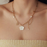 Collier en acier inoxydable doré, maillons, avec grande fleur nacre, petite fleur dorée, papillon, perle et strass.