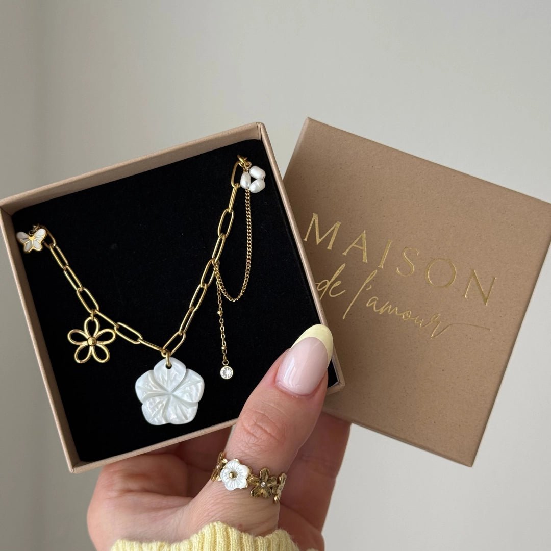 Collier acier inoxydable doré avec grand pendentif fleur blanche, petite fleur or, papillon et perles, dans une boîte cadeau.