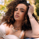Collier en acier inoxydable doré avec pendentifs soleil, pièce, cœur bleu et perles, porté par une femme.