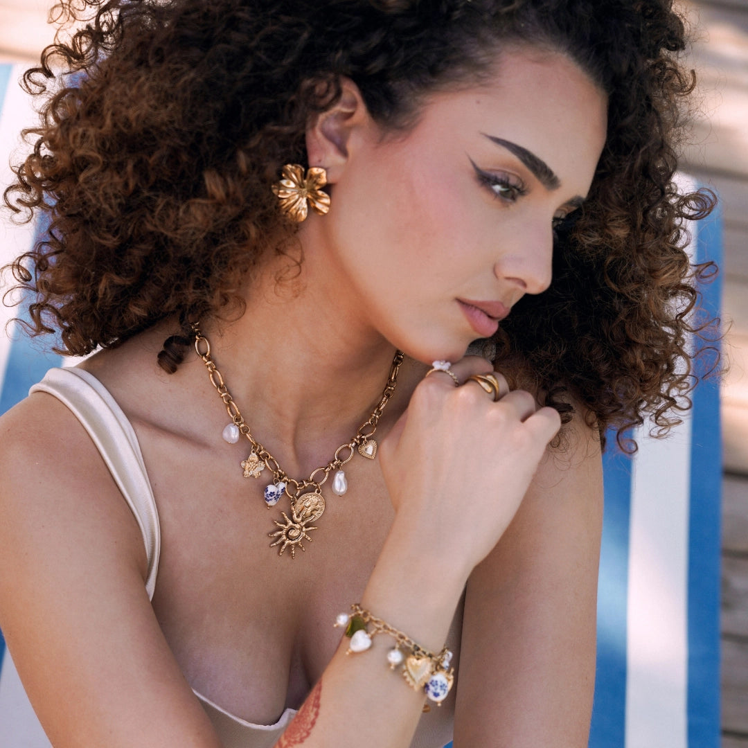 Collier en acier inoxydable doré avec charms: médaillon, soleil, coeurs, perles et céramique bleue.