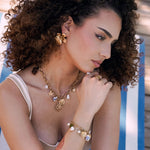 Collier en acier inoxydable doré avec charms: médaillon, soleil, coeurs, perles et céramique bleue.