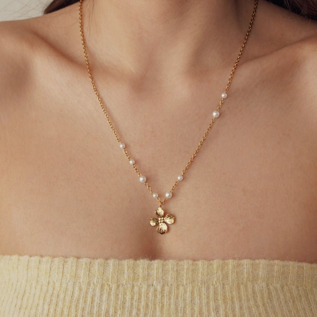 Collier acier inoxydable doré maillons fins, perles blanches et pendentif fleur 4 pétales texturée sur une femme.
