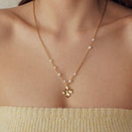 Collier acier inoxydable doré maillons fins, perles blanches et pendentif fleur 4 pétales texturée sur une femme.