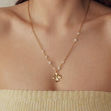 Collier acier inoxydable doré maillons fins, perles blanches et pendentif fleur 4 pétales texturée sur une femme.