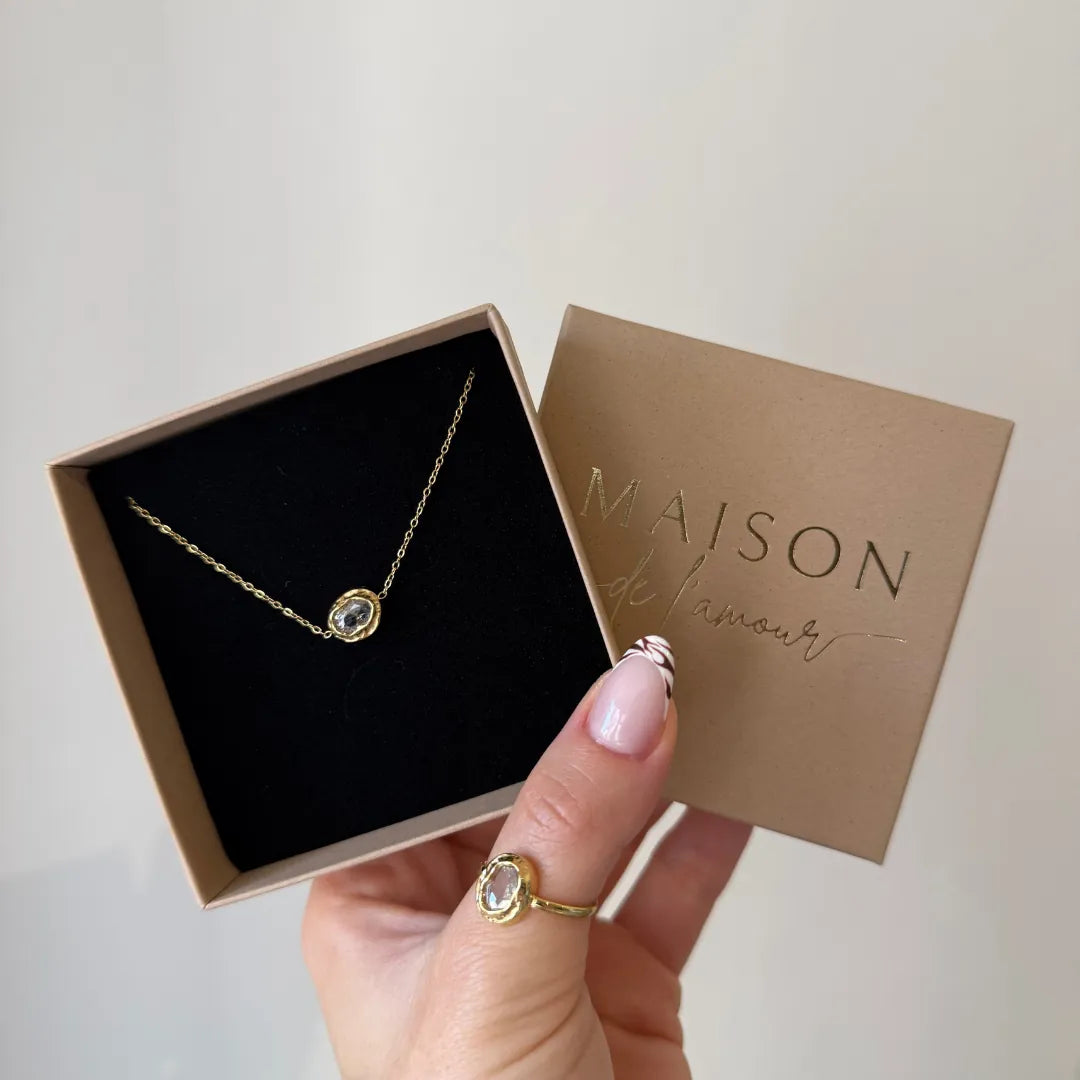 Collier en acier inoxydable doré avec un strass en zirconium dans un coffret cadeau tenu par une main avec une bague