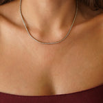 Collier rivière tennis en acier inoxydable doré, serti de petits zircons brillants, porté au cou.