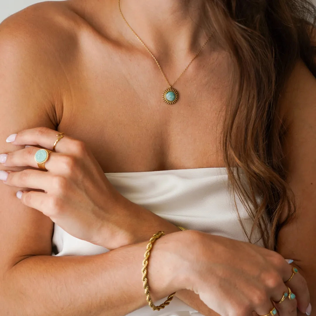 Collier fin en acier inoxydable doré avec pendentif soleil et pierre naturelle Amazonite porté sur le décolleté.