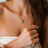 Collier fin avec pendentif soleil en Amazonite et acier inoxydable doré, porté par une femme. Trois bagues en acier