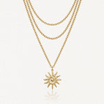 Collier trois rangs en acier inoxydable doré, pendentif soleil stylisé avec spirale et rayons.