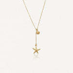 Collier lariat acier inoxydable doré avec pendentifs coquillage et étoile de mer, sur fond blanc.