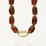 Collier MAISON DE L'AMOUR avec grosses perles marron effet écaille et pièce centrale dorée en acier inoxydable sur fond blanc.