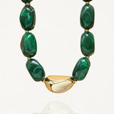 Collier MAISON DE L'AMOUR avec grosses perles vertes marbrées effet malachite et pièce centrale dorée en acier inoxydable sur fond blanc.