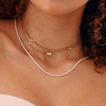 Colliers superposés: 2 en acier inoxydable doré avec perles pendantes, 1 collier de perles fines sur le cou d'une femme.