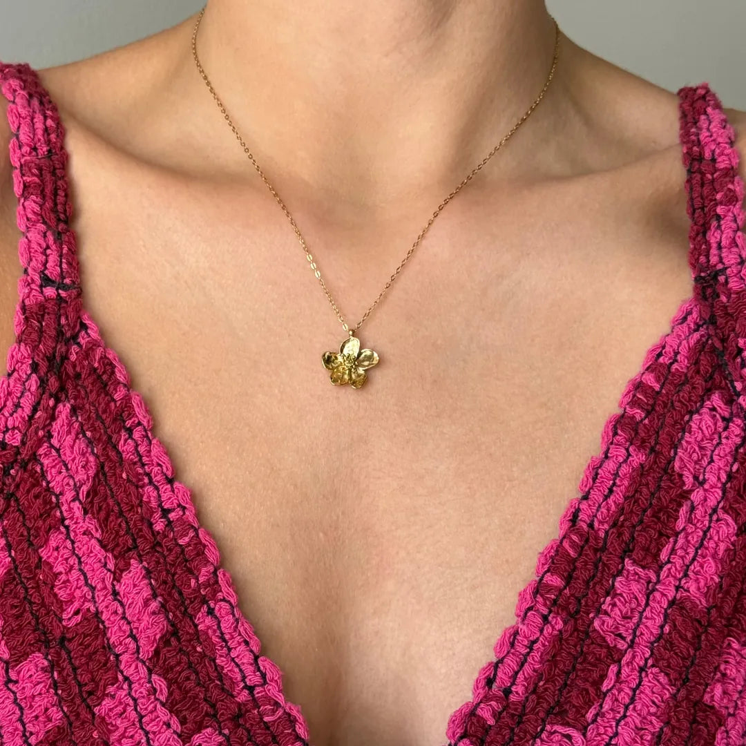 Collier en acier inoxydable doré, pendentif fleur détaillé, porté sur un décolleté.