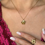 Collier en acier inoxydable doré, pendentif fleur. Porté par une femme, avec une bague fleur assortie visible à sa main.