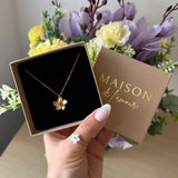 Main tenant un écrin "MAISON de l'amour" avec collier en acier inoxydable doré à pendentif fleur et une bague en nacre au