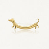 Broche chien teckel en acier inoxydable doré. L'épingle à nourrice est visible au dos, sur fond clair.