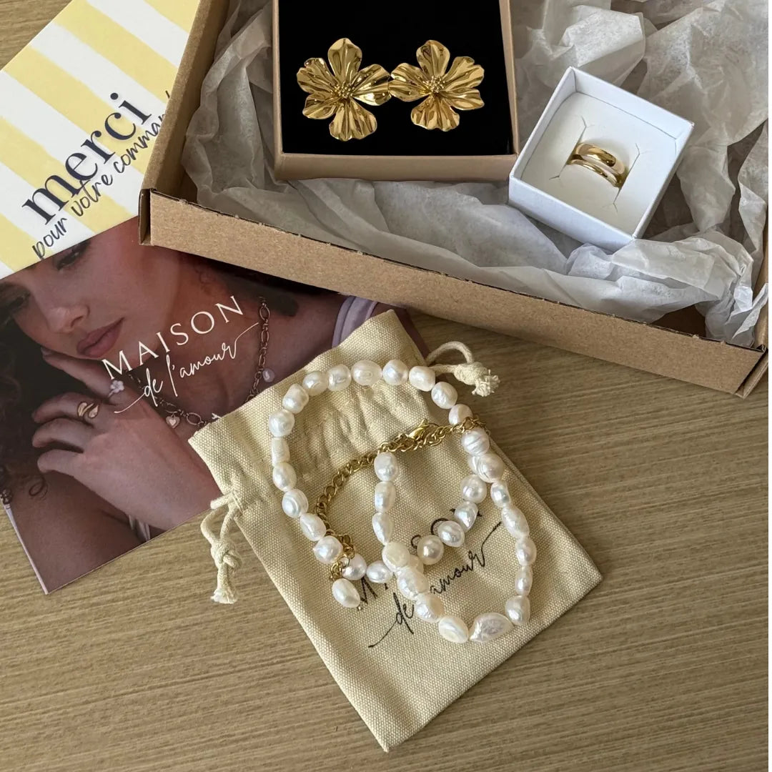 Collier de perles d'eau douce irrégulières et acier doré sur un pochon. Dans un coffret ouvert : boucles d'oreilles et bague