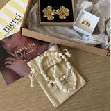 Collier de perles d'eau douce irrégulières et acier doré sur un pochon. Dans un coffret ouvert : boucles d'oreilles et bague