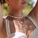 Collier en acier inoxydable doré, chaîne fine avec pendentif coquillage et perles, porté par une femme.