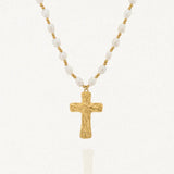 Collier avec une chaîne composée de perles blanches baroques et de petites billes dorées. Le pendentif est une croix dorée à la surface texturée et irrégulière.