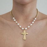 Collier à perles baroques blanches et perles dorées, pendentif croix martelée doré, porté sur un cou.
