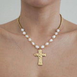Collier à perles baroques blanches et perles dorées, pendentif croix martelée doré, porté sur un cou.