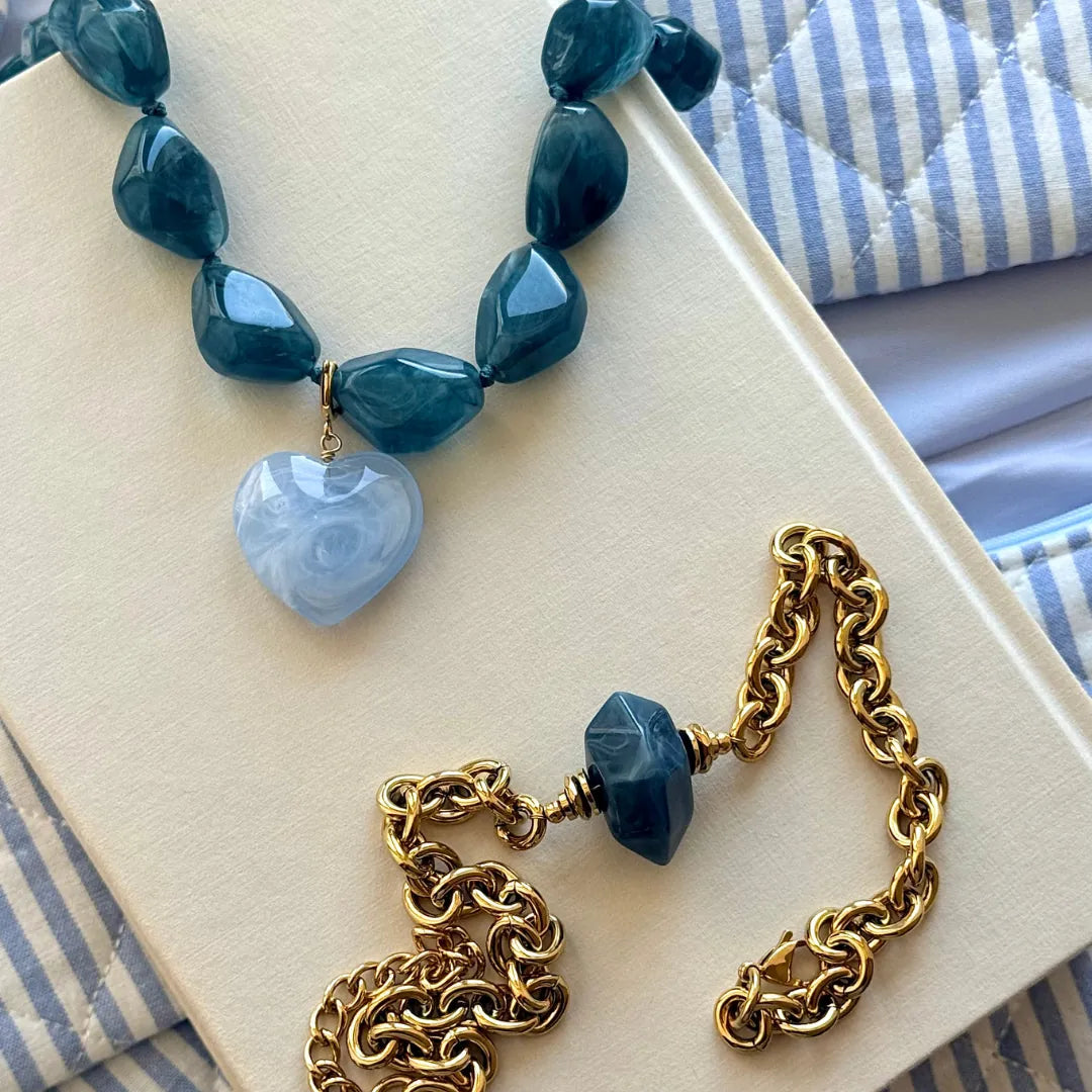 Collier de perles de résine bleu foncé, pendentif cœur en résine bleu clair marbrée, et fermoir en acier inoxydable doré.