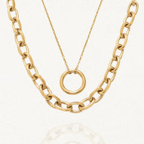 Double collier doré en acier inoxydable. Il se compose d'une chaîne épaisse à maillons ovales et d'une chaîne fine avec un pendentif anneau lisse.