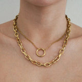 Colliers dorés superposés sur le cou. Un collier chaîne épaisse et un collier chaîne fine avec pendentif anneau.