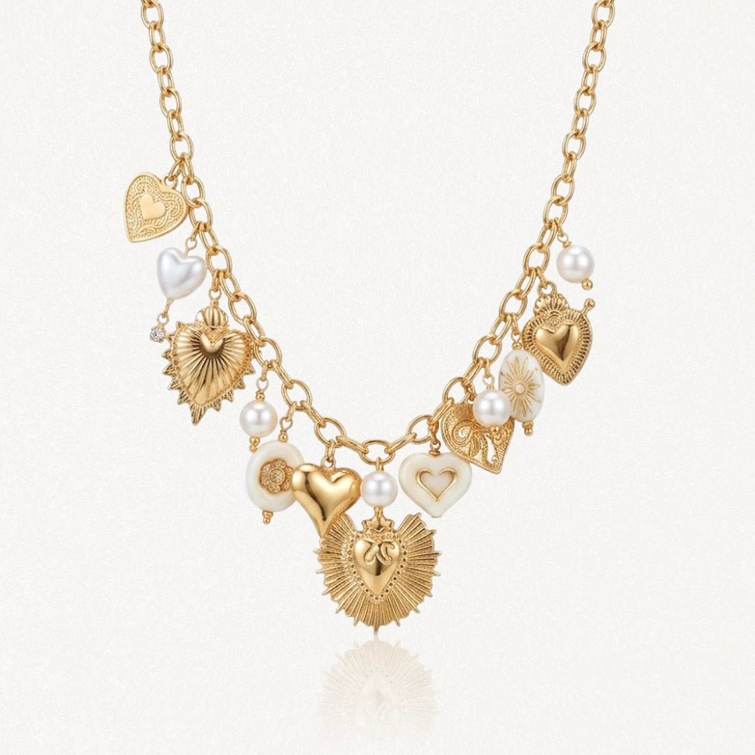 Collier en acier inoxydable doré, chaîne à maillons, avec multiples pendentifs cœurs, perles et éléments émaillés blancs.