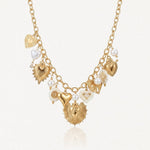 Collier en acier inoxydable doré, chaîne à maillons, avec multiples pendentifs cœurs, perles et éléments émaillés blancs.