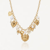 Collier en acier inoxydable doré, chaîne à maillons, avec multiples pendentifs cœurs, perles et éléments émaillés blancs.
