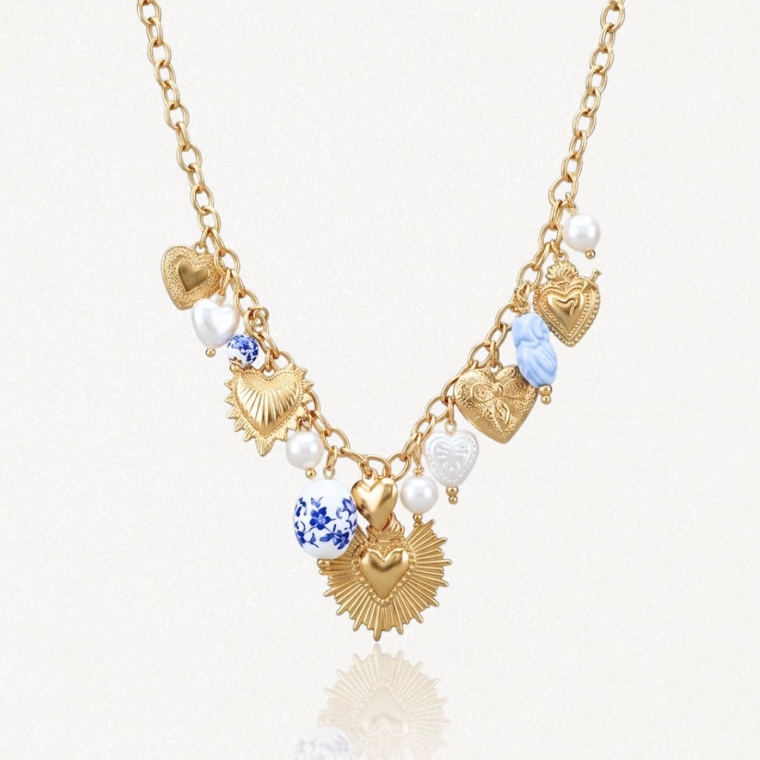 Collier en acier inoxydable doré, multiples pendentifs cœurs sacrés et texturés, perles et charms bleu/blanc.