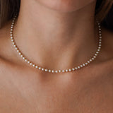 Collier ras-de-cou en perles blanches et billes d'acier inoxydable doré, porté sur le décolleté.