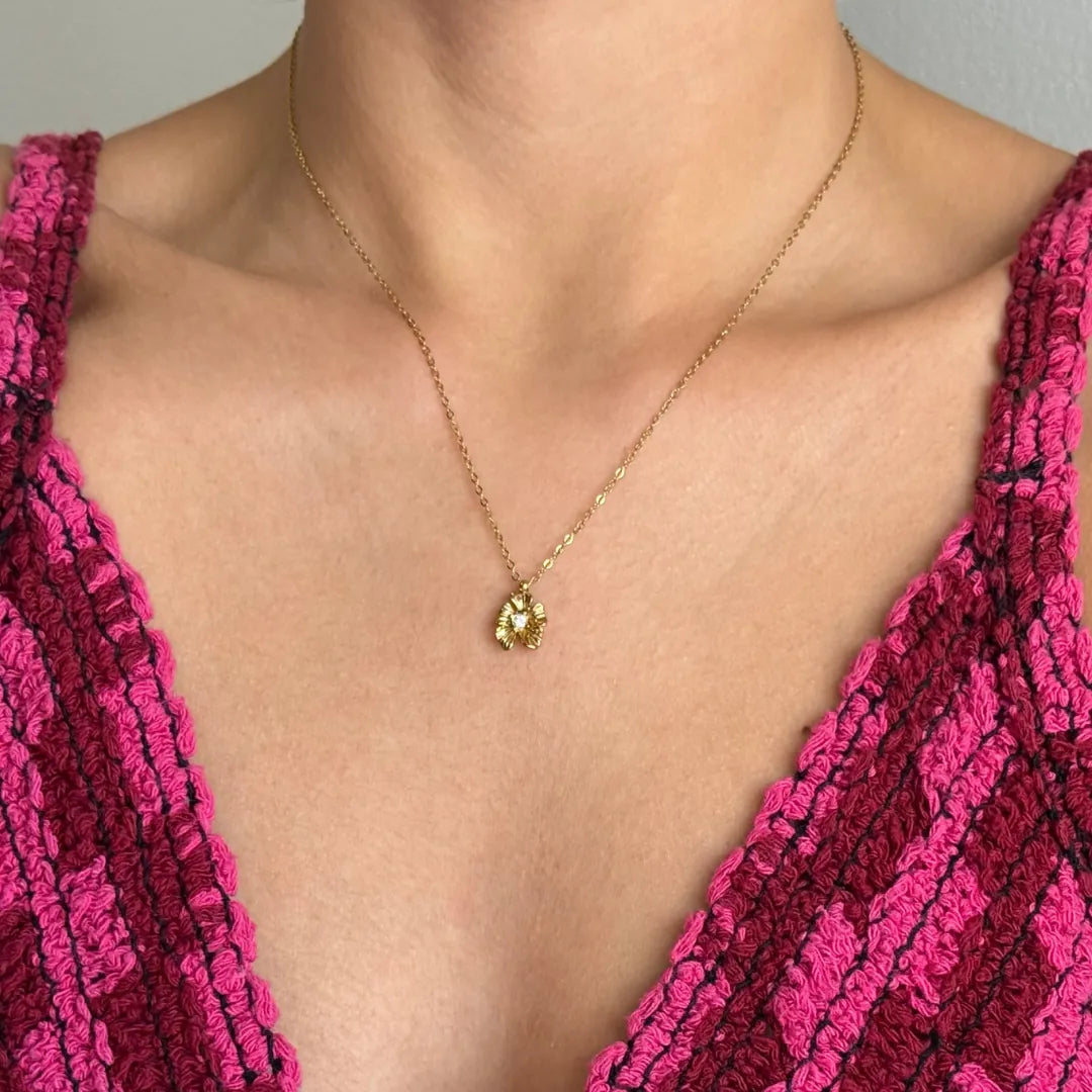 Collier en acier inoxydable doré avec pendentif fleur et son petit détail brillant central, porté au cou.