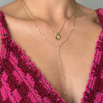 Deux colliers en acier inoxydable doré superposés. L'un avec un pendentif fleur et strass, l'autre en Y avec des strass.