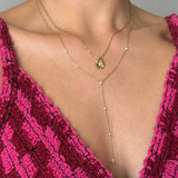Deux colliers en acier inoxydable doré superposés. L'un avec un pendentif fleur et strass, l'autre en Y avec des strass.
