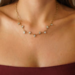 Collier vague en acier inoxydable doré, orné de zircons multiformes sertis clos, porté sur le décolleté d'une femme.