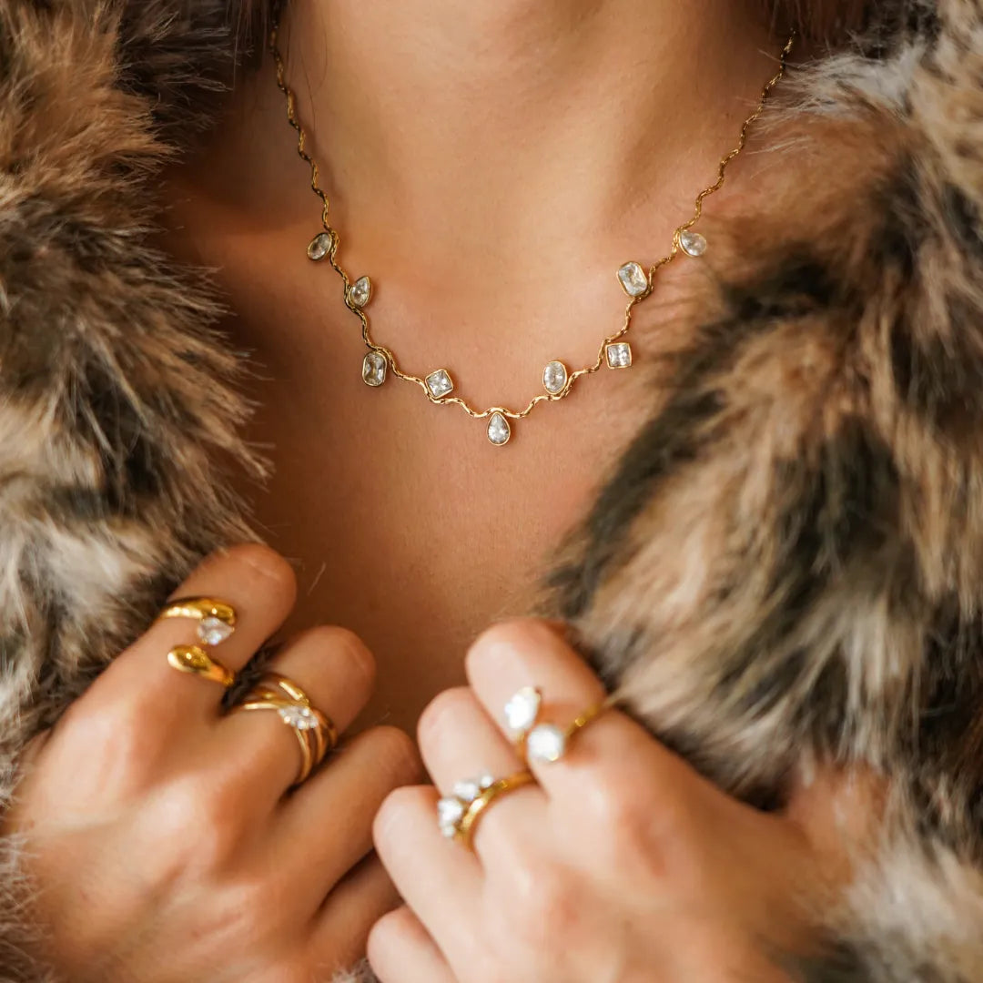 Collier vague en acier inoxydable doré, orné de zircons multiformes sertis clos, porté par une femme en fourrure.