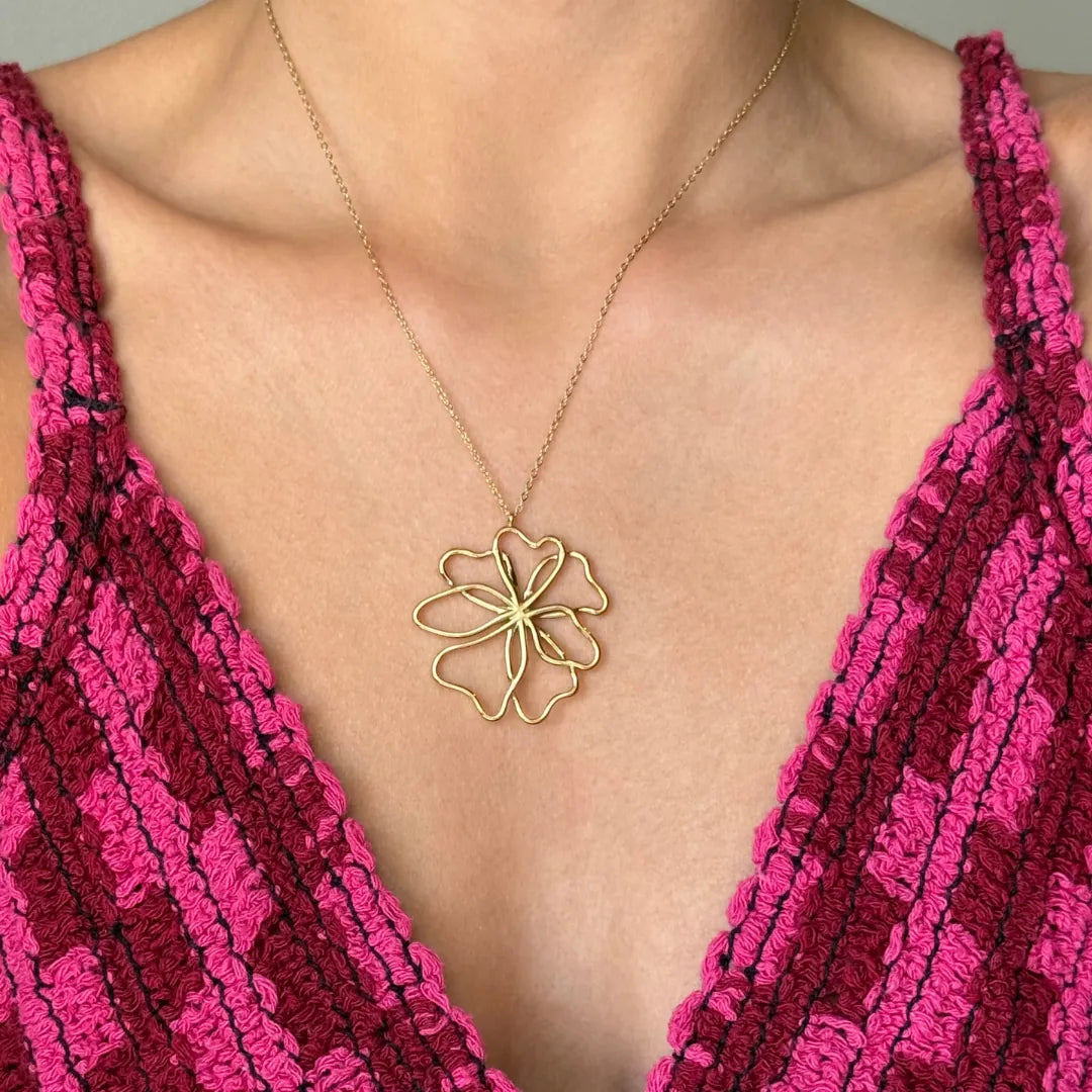 Collier en acier inoxydable doré avec un pendentif fleur ajouré, porté sur un décolleté.